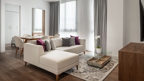 A modern living room with a sofa, coffee table, and a dining area with chairs and a table. - Master Suite DLX (Heredia)