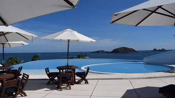 Un espace aménagé au bord de la piscine, avec des parasols, des chaises et une vue sur l’océan.