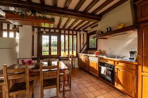 A rustic kitchen with wooden cabinets, a tiled floor, and a dining area with a wooden table and chairs.