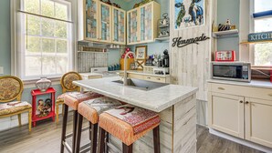 A kitchen with a marble countertop, wooden chairs, and a red stool. There are cabinets with decorative paper, a microwave, and a sign that says "Happin'". - Grand Historic Home w/ Yard & Deck in High Point! (High Point)
