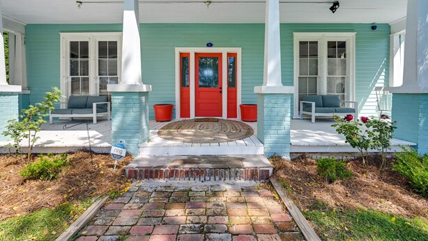 A house with a porch, a red door, and a brick pathway leading to the entrance. - Grand Historic Home w/ Yard & Deck in High Point! (High Point)