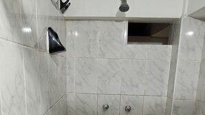 Une zone de douche carrelée, équipée d’un pommeau de douche et de deux robinets de réglage.