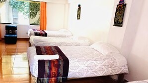Une chambre d’hôtel avec trois lits, un plancher en bois, une fenêtre avec des rideaux et un tableau accroché au mur.