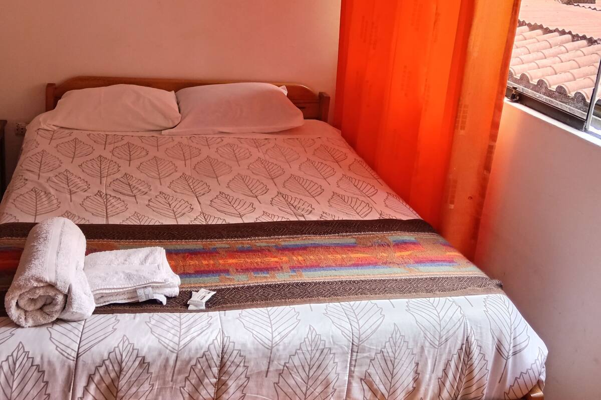 Un lit simple avec une couvre-lit à motifs, un oreiller blanc et une serviette enroulée sur le côté.