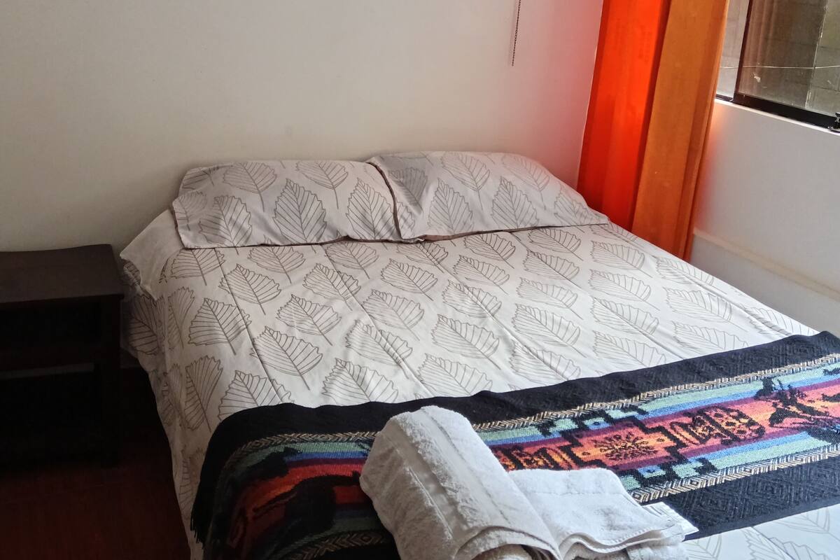 Une chambre à coucher avec un lit, une table de chevet, une prise électrique et une fenêtre avec des rideaux orange.