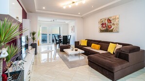 A modern living room with a brown sofa, white coffee table, and a dining area in the background. - Apartments Sandito - Two Bedroom Apartment with Terrace and Sea View (Mlini)