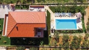 An aerial view of a house with a red-tiled roof, a swimming pool, and a garden area.