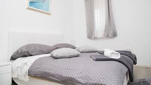 A bedroom with a bed, pillows, a blanket, a framed picture, and a window with curtains.