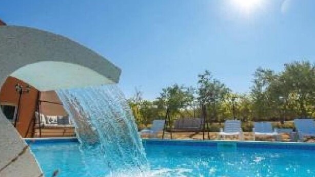 A swimming pool with a water feature, surrounded by lounge chairs and trees.