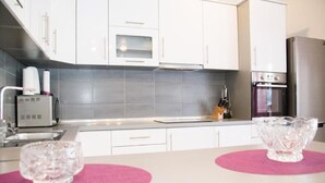A modern kitchen with white cabinets, a stainless steel countertop, a built-in oven, and a refrigerator.