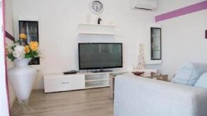 A modern living room with a flat-screen TV, white furniture, and a clock on the wall.