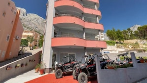 Un immeuble à plusieurs étages doté de balcons, d’un tapis rouge et de quads garés devant.