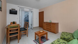 A living room with a wooden dining table, chairs, a small coffee table, a sofa, a TV, and a cabinet.