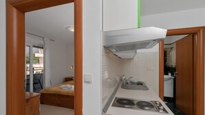A compact kitchen with a stove, sink, and a small dining area with a bed.