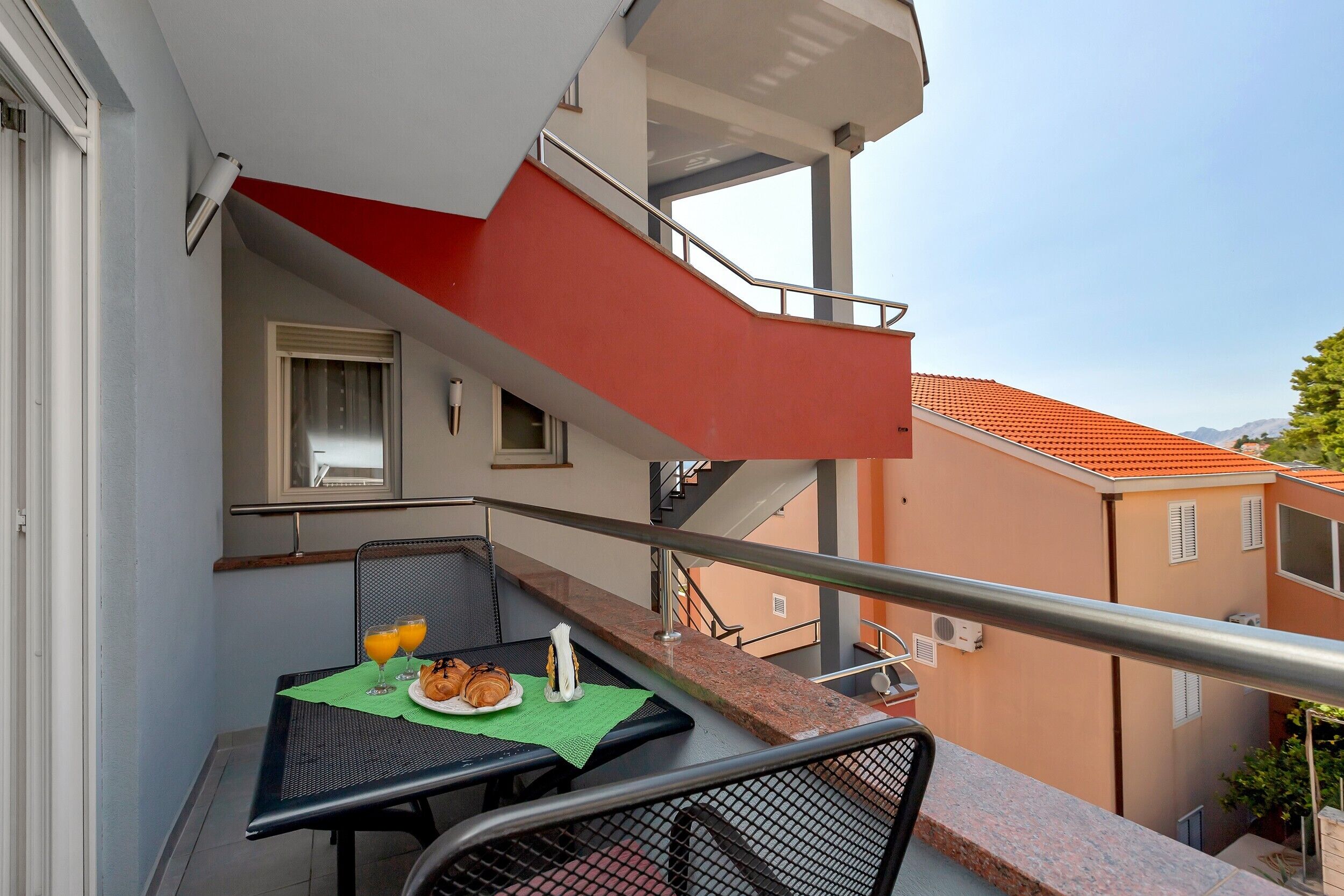 Un balcón con mesa dispuesta para el desayuno, una silla y un toldo rojo.
