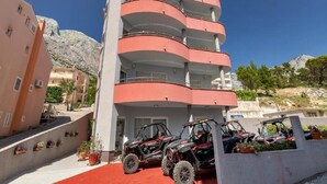 Un edificio de varios pisos con balcones, alfombra roja y vehículos todo terreno estacionados al frente.