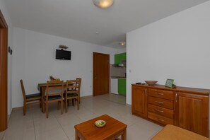 A modern living room with a dining area, a kitchen in the background, and a wooden cabinet with drawers.