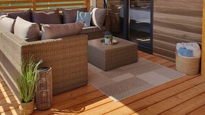 Un espace extérieur aménagé, abrité et doté d'un canapé en osier et d'une petite table, d'une porte-fenêtre coulissante et d'une terrasse en bois.