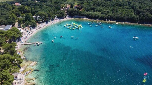 Vue aérienne d’une zone côtière avec des eaux turquoise limpides, une plage de sable et quelques bateaux dispersés.