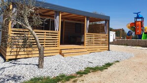 Une cabane en bois avec un porche couvert, une allée en gravier et, au fond, une aire de jeux.