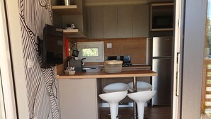 Une cuisine moderne avec un plan de travail en bois, un four encastré et un réfrigérateur en acier inoxydable. On y trouve deux tabourets de bar blancs et une fenêtre qui laisse entrer la lumière naturelle.