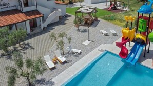 Un espace piscine avec un toboggan, des chaises longues et un bâtiment portant une enseigne.