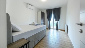 Una camera da letto moderna con un letto, un comodino, un condizionatore d'aria e vista sull'esterno attraverso una finestra con tende.