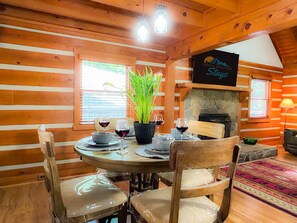 A wooden cabin interior with a dining table set for four, surrounded by wooden chairs. A stone fireplace and a sign reading "Smoky Mountain Stay" are visible. - Smoky Mountain Cabin w/ Hot Tub & View | Private - Cherokee & Bryson City (Whittier)