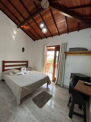 A bedroom with a bed, a desk, a refrigerator, and a door leading to an outdoor area.