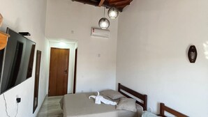 A room with a wooden ceiling, a bed, a sofa, a TV, and an air conditioning unit. - Pousada Luz da Lua (Búzios)