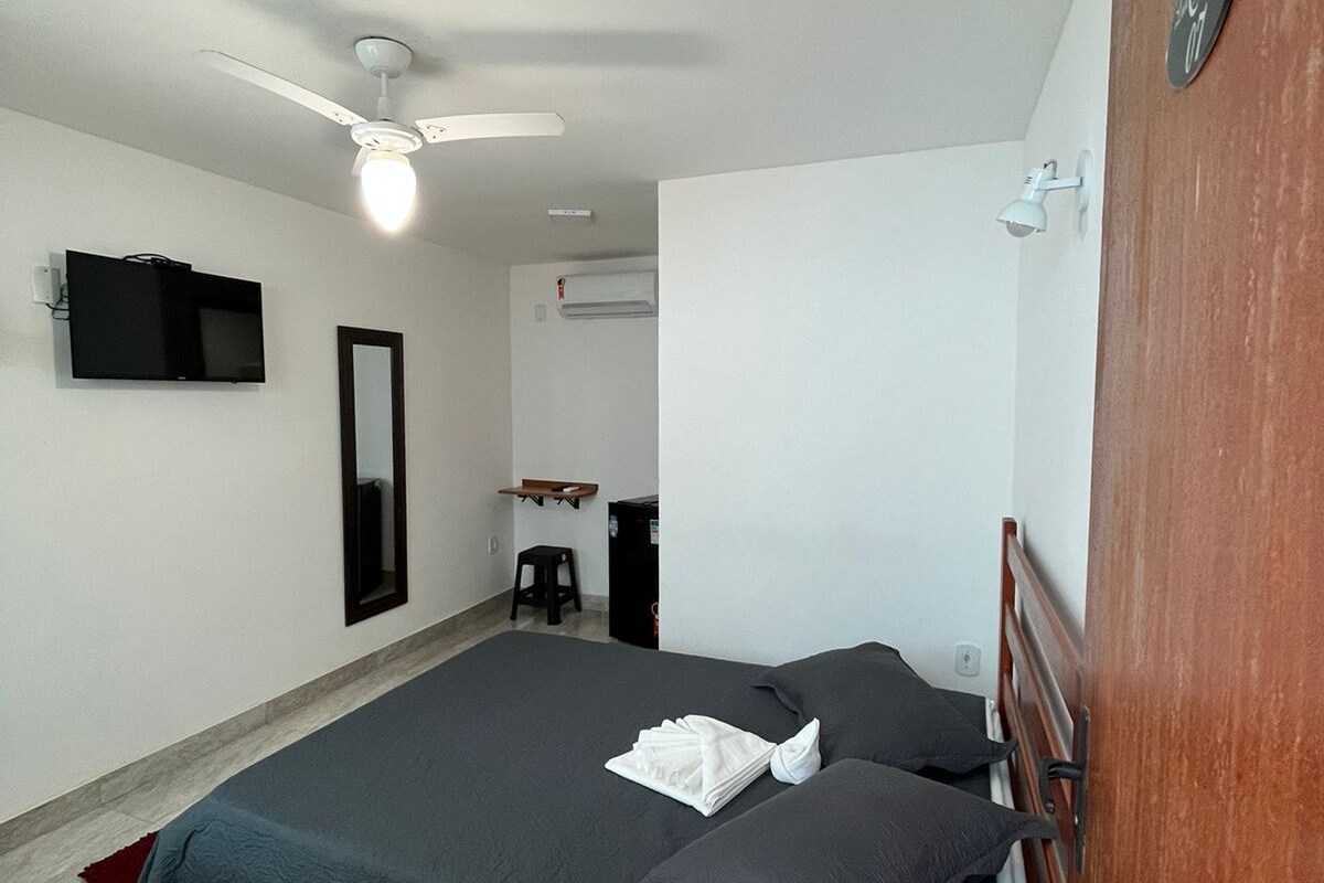 A bedroom with a bed, a ceiling fan, a TV, a mirror, and a wooden door.