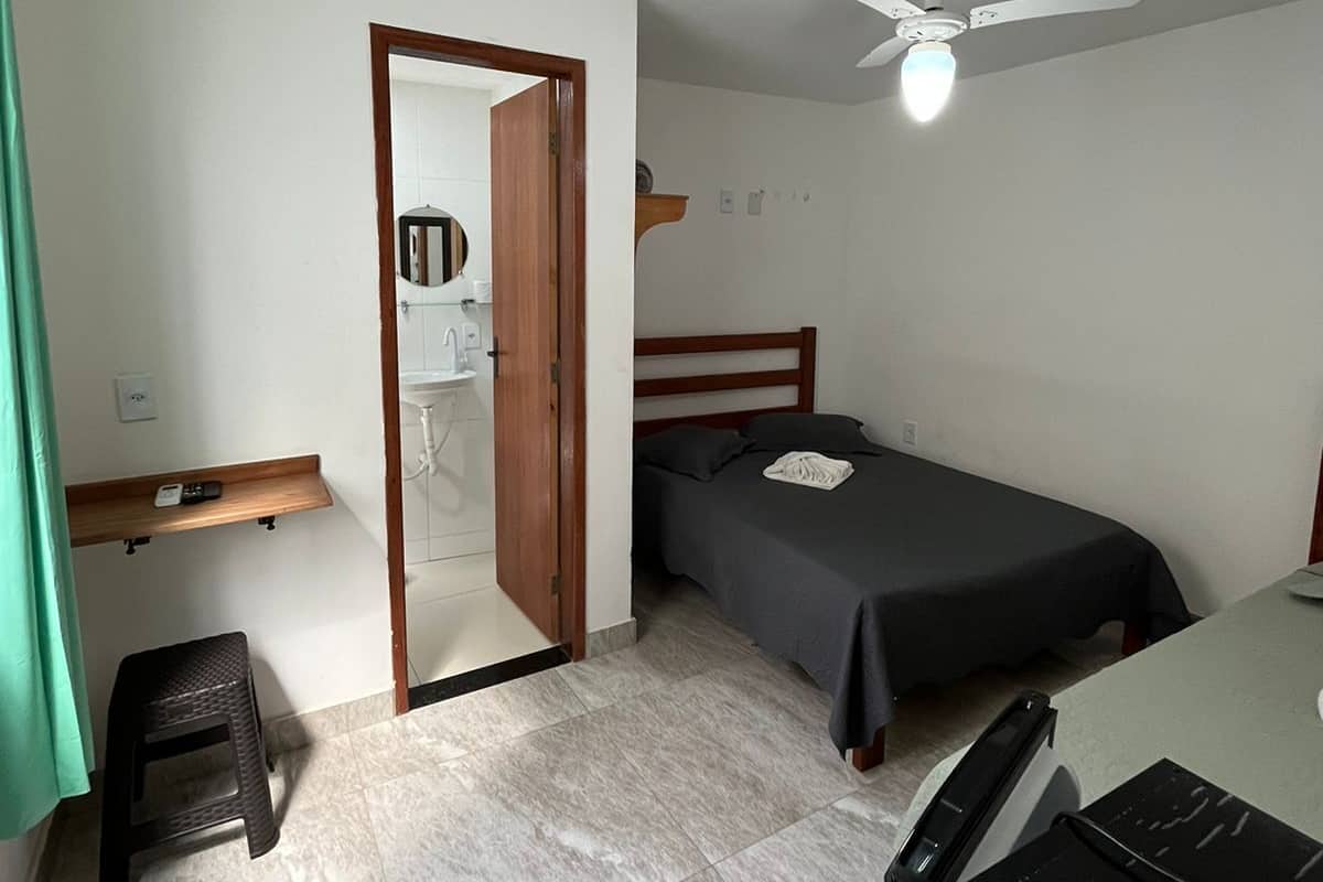 A small, clean room with a bed, a desk, a chair, and a ceiling fan.