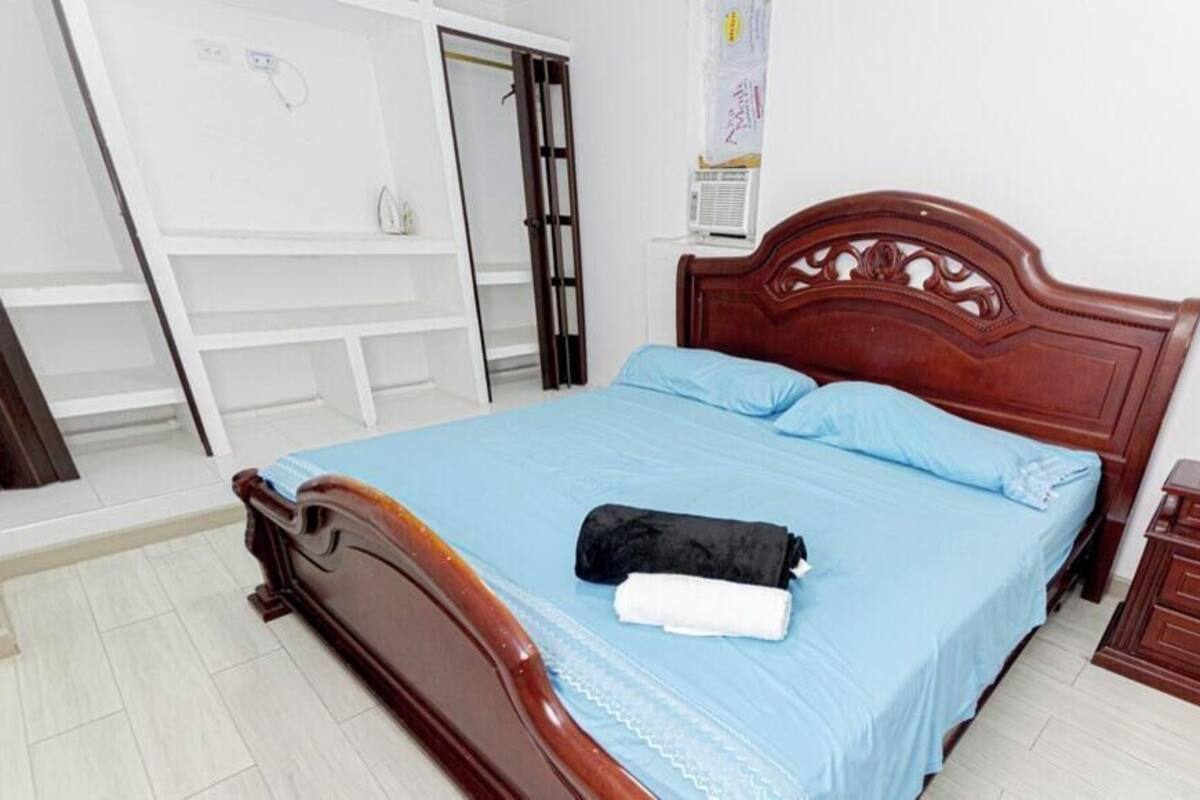 A bedroom with a wooden bed, a blue bedspread, a white towel, a wooden nightstand, and a white wardrobe.