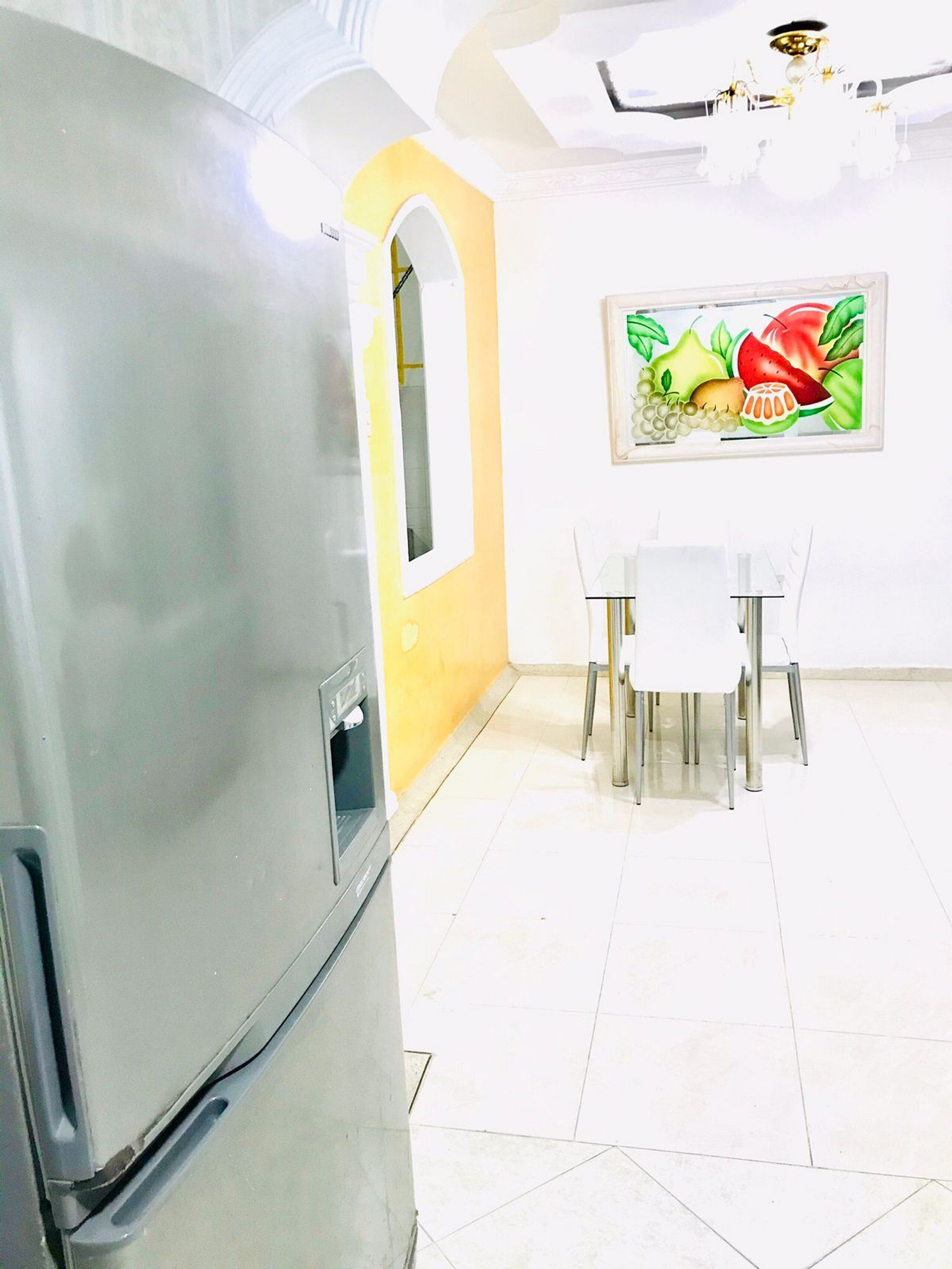 Une cuisine équipée d’un réfrigérateur, d’une table à manger avec des chaises et d’une décoration murale sur le thème des fruits.