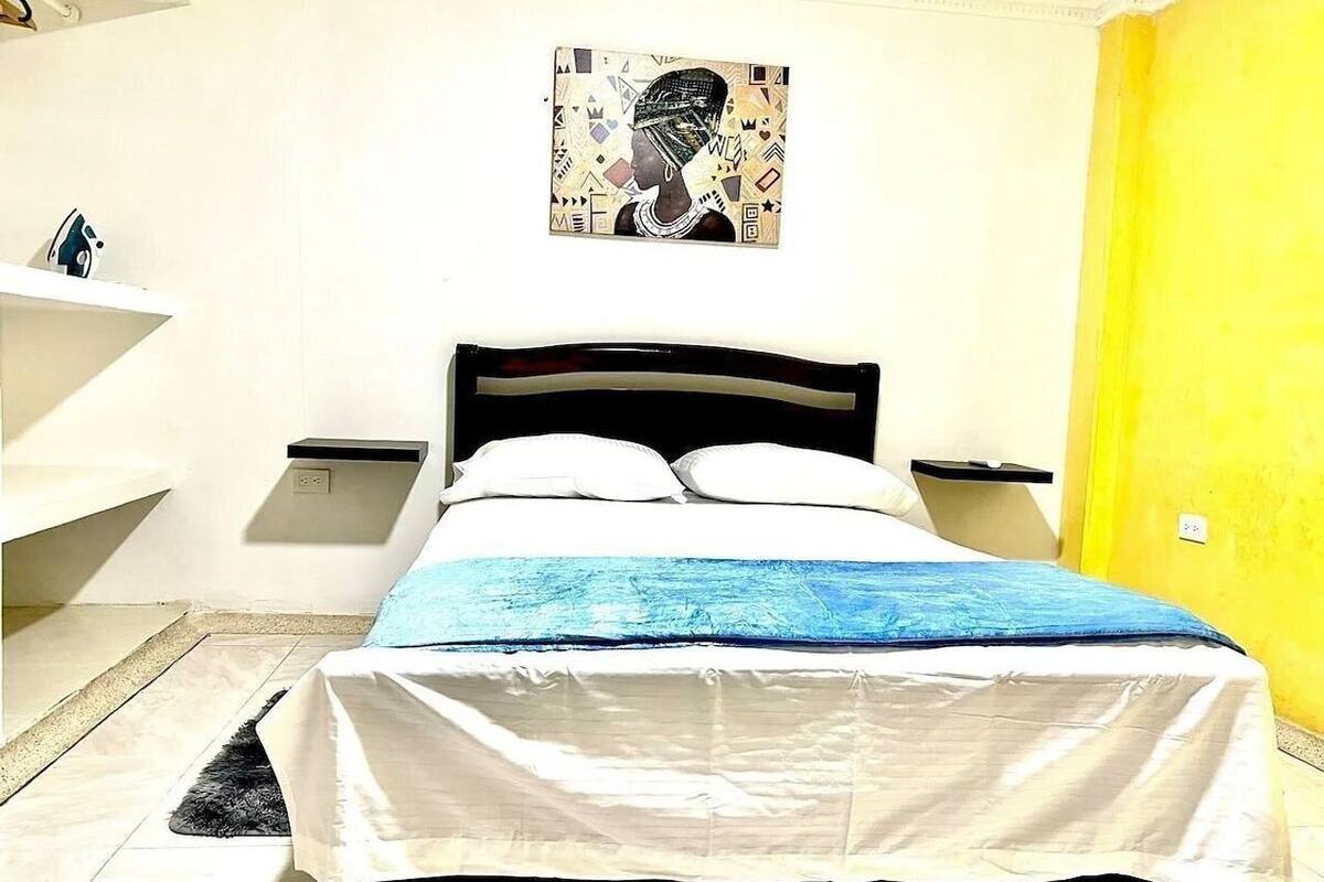 A bed with a blue blanket, a wall-mounted picture, and a yellow door.