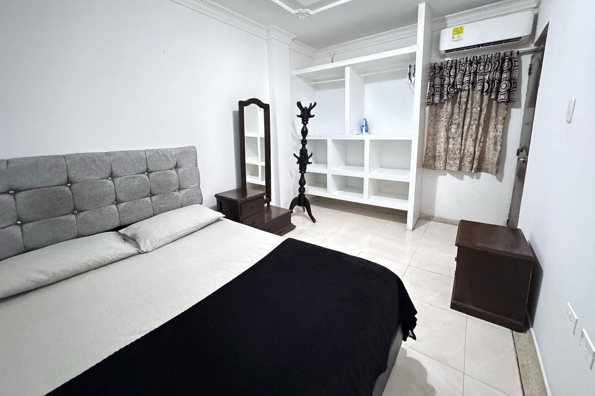 A bedroom with a bed, a wardrobe, a mirror, and a tripod stand.