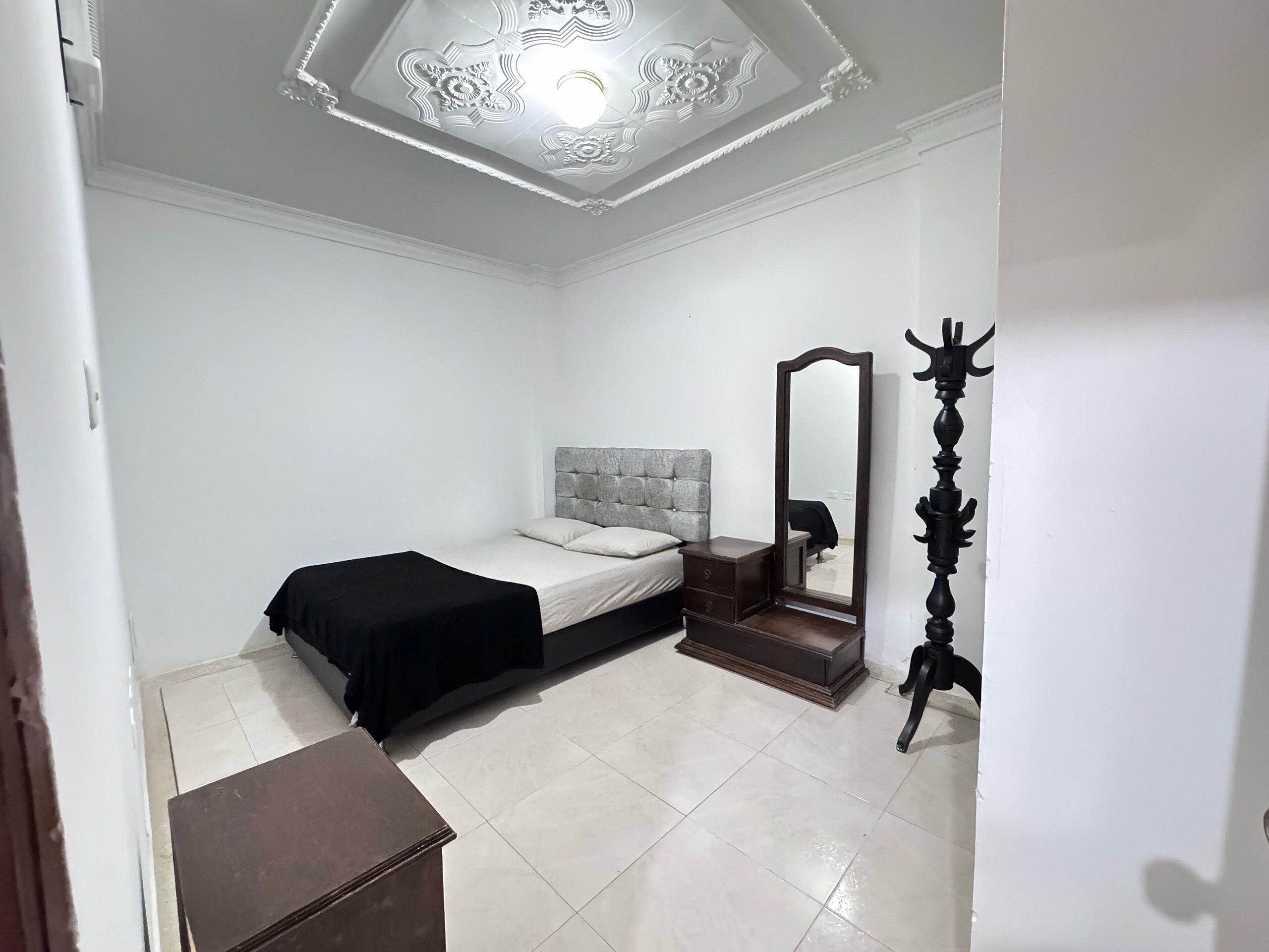 Ein Schlafzimmer mit einem Bett, einem Schminktisch, einem Spiegel und einer Deckenleuchte.
