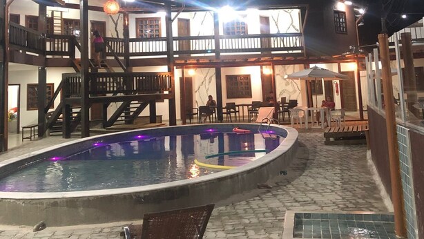 A pool area with a wooden deck, a lounge chair, and a staircase leading to an upper level. - Hotel Porto Brasília (Porto Seguro)