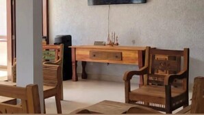 A living room with a television mounted on the wall, wooden furniture, and a small table with decorative items. - Hotel Porto Brasília (Porto Seguro)