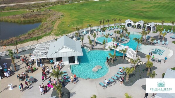 A resort with a large swimming pool, outdoor seating areas, and a golf course in the background.