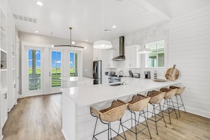 A modern kitchen with white cabinetry, a large island with bar stools, and a view of the outdoors through glass doors.
