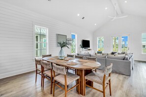 A spacious living room with a large round table, comfortable seating, and a flat-screen TV mounted on the wall.