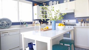 A kitchen with white cabinets, a blue vase with flowers, a bowl of lemons, and a blue stool.