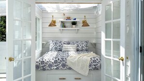 A cozy bedroom with a bed, a small shelf with decorative items, and two wall-mounted lamps.