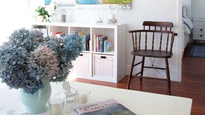 A cozy room with a white bookshelf, a wooden chair, a table with a vase of flowers, and a colorful painting on the wall.