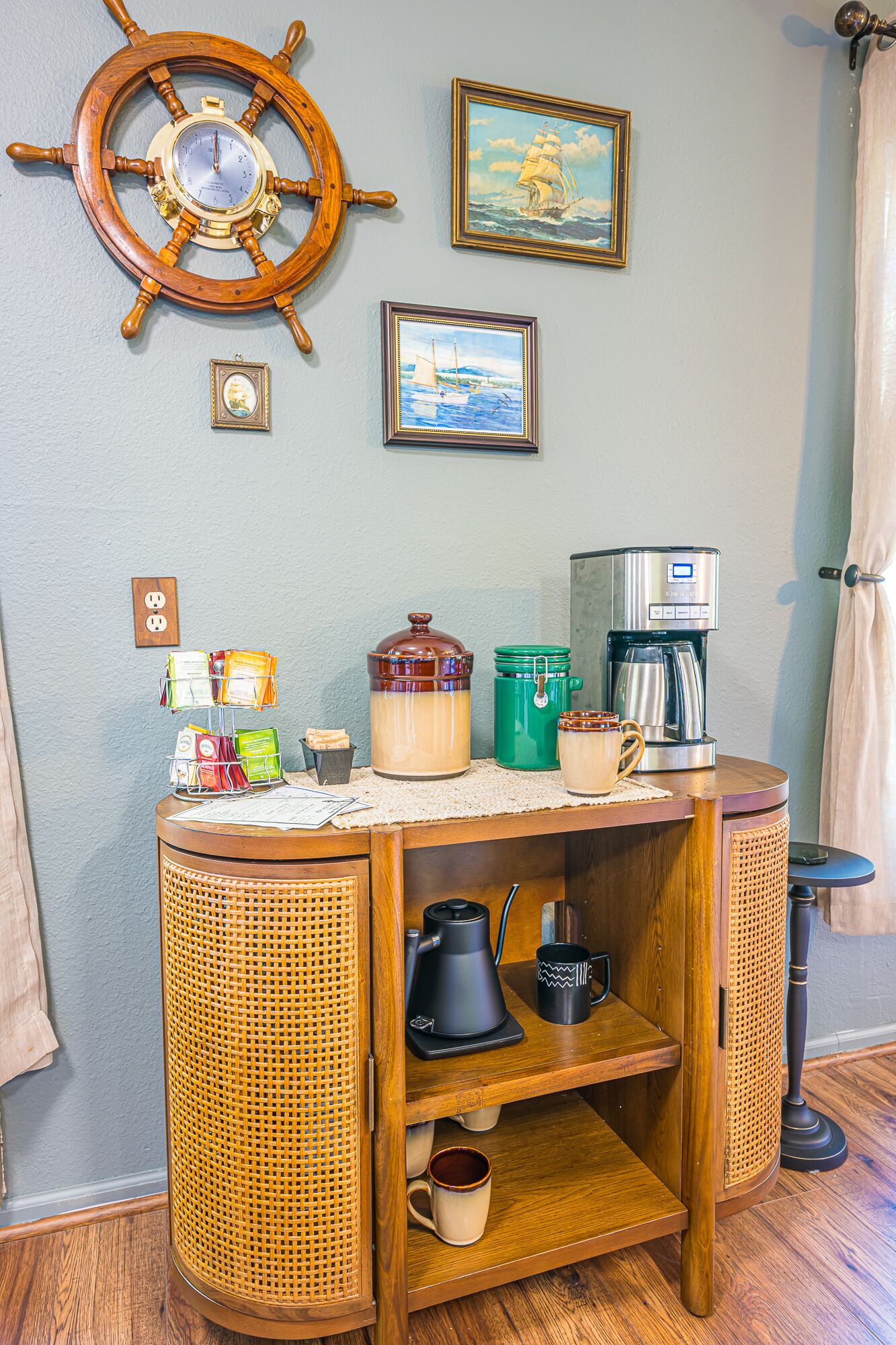 A cozy room with a wooden coffee station, a ship's wheel, and nautical-themed artwork.