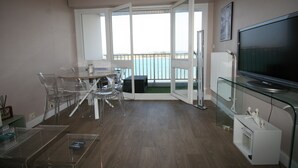 A modern living room with a glass coffee table, a flat-screen TV, and a balcony with a view of the sea. - Vue sur mer Epoustouflante (Trégastel)