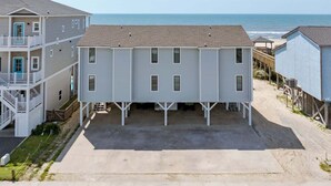 A beachfront property with a two-story building, a covered parking area, and a view of the ocean.