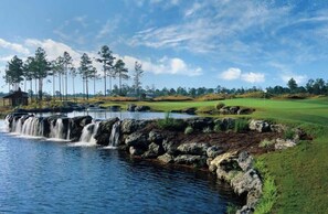 Ein Golfplatz mit Wasserfall, Bäumen und einem kleinen Gebäude.