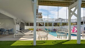 A covered outdoor area with a pool, lounge chairs, and a swing set.